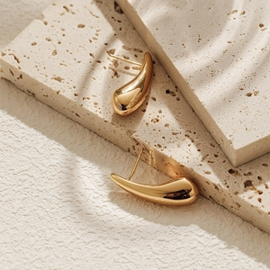 Polished 18K gold teardrop earrings shown on stone plate with elegant shadow play