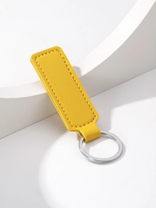 Detailed view of yellow leather keychain with silver metal ring on a white stone pedestal
