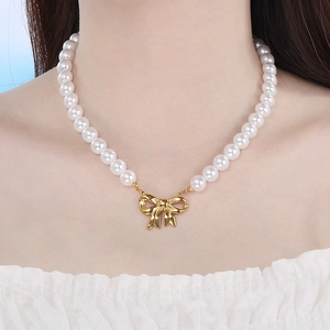 Close-up of pearl necklace with a polished gold bow pendant on woman neck