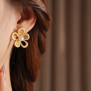 Gros plan d'une boucle d'oreille fleur évidée dorée avec perle portée par un modèle