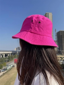 Outdoor shot of a bright pink cotton bucket hat with metal eyelets worn by a model