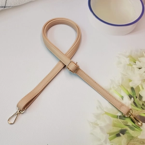 Détail de la bandoulière réglable en cuir beige avec boucles en métal doré poli
