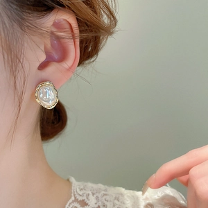Detail of irregular baroque pearl earrings with golden frames on a female model