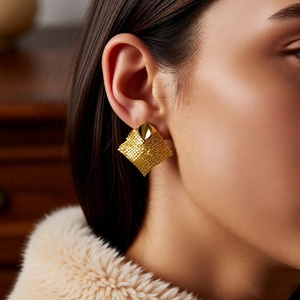 Close-up of golden rhombus mesh earrings worn by a model in soft warm lighting