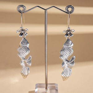 Orecchini pendenti a forma di pesce e fiore in argento su espositore in metallo
