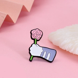 Detail of cartoon enamel pin featuring a white cat paw holding a pink rose flower