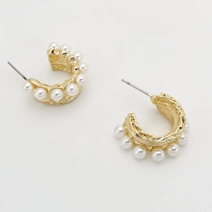 Macro shot of gold-plated C-shaped earrings with multiple pearls on a clean background