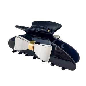 Detail view of a black acetate hair claw clip featuring a white bow and gold metal accent