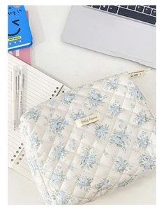 Dettaglio del beauty case in tessuto trapuntato bianco con motivi floreali blu