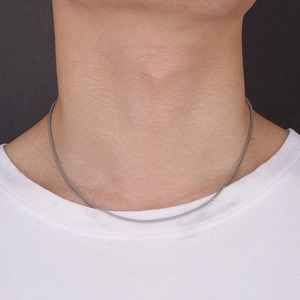 Detail of silver woven stainless steel necklace worn on a neck over a white T-shirt