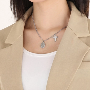 Detailed view of silver oval religious medal and cross pendant on a delicate chain