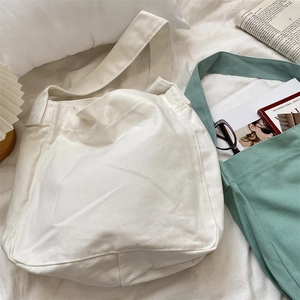 Primo piano di borse tote in tela beige e grigio-verde con spalline larghe su lino bianco