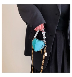 Mini sac cœur bleu métallisé porté sur un blazer noir pour illustrer la taille compacte