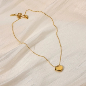 Polished golden heart pendant on a thin snake chain lying on a silk fabric