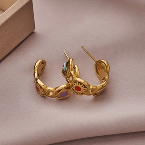 Close-up of gold C-shaped earrings with colorful enamel sun and evil eye charms