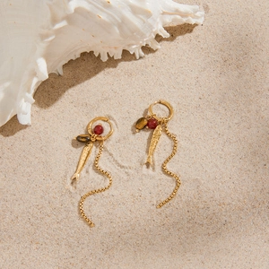 Detail of 18K gold fish earrings with tassel and red beads on a sandy beach setting