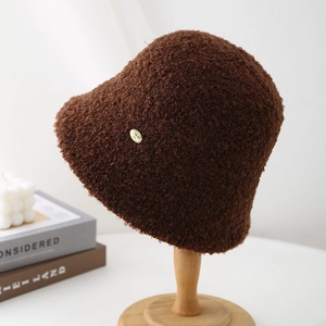 Detailed texture of brown fleece bucket hat with a gold metal plate on a wooden stand