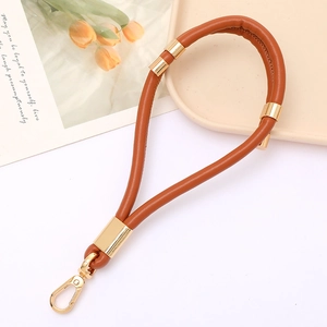 Detail of brown PU leather wristlet strap with gold rings and swivel clasp on ceramic tray