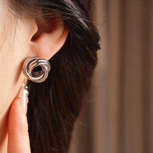 Gros plan de boucles d'oreilles nœud argentées minimalistes portées par un mannequin
