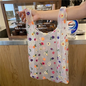 Detailed embroidery of colorful flowers on white mesh tote bag held by hand