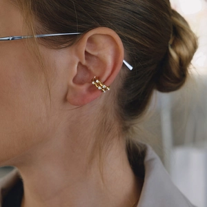 Detailed view of 18K gold plated wavy ear cuff with sparkling zircons on female ear
