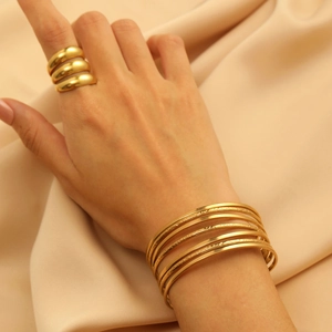 Close-up of golden multi-layer bracelet and wide band ring set on champagne silk background