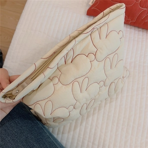 Macro detail of quilted rabbit embroidery on cream cosmetic bag with smooth metal zipper