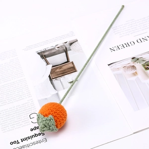 Close-up of hand-knitted orange persimmon flower with green stem on a white magazine background