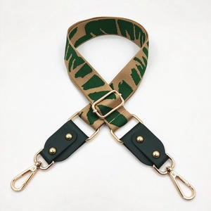 Close-up of beige and green jacquard wide strap with leather ends and gold metal buckles