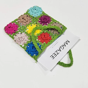 Handmade crochet tote bag with colorful floral patterns and green knitted handles