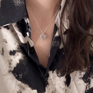 Detail of a 925 sterling silver heart necklace worn against a black and white patterned shirt