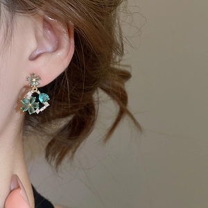 Detailed close-up of 18k gold-plated floral earrings with green and clear crystals