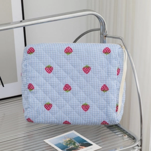 Détail du motif fraise sur le tissu matelassé à carreaux bleus de la trousse de maquillage