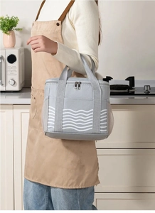Grey insulated lunch bag with white wave pattern being held in a modern kitchen setting