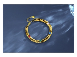 Close-up of golden Cuban chain bracelet with colorful zircons on water ripple background