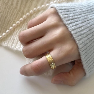 Close-up of minimalist gold three-band ring worn by model with cozy knit backdrop