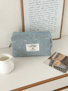 Blue denim storage bag with bow print and zipper closure on a cozy desktop setting