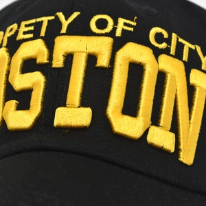 Detailed close-up of yellow 3D embroidery showing Boston text on a black cotton baseball cap
