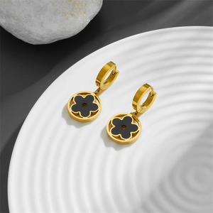 Détails des boucles d'oreilles trèfle doré avec incrustation noire sur plateau céramique