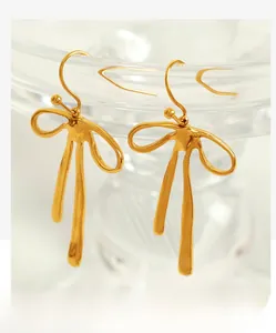 Detail of gold bow earrings with liquid texture hanging on a glass rim in soft light