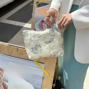 Close-up of white plush cosmetic bag featuring blue lace butterfly patterns and brand label