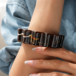 Dettaglio di un bracciale a onde in acrilico marrone con trama bianca indossato da una modella