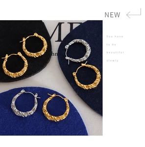 Macro shot of gold and silver twisted hoop earrings on sleek navy display pedestals