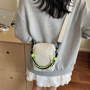 Detail of beige canvas crossbody bag with contrast green and black braided handle