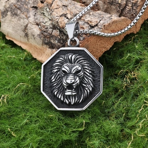 Detailed view of silver lion head hexagonal pendant on green moss with steel box chain