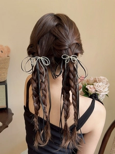 Detail of silver bow hair clips with long black ribbons on braided double ponytails