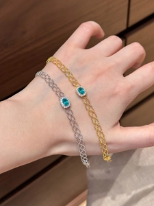 Detail of gold and silver bracelets with green gemstones on a braided hollow chain