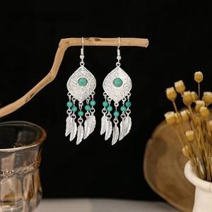 Detail of silver feather tassel earrings with turquoise beads on a wooden stand
