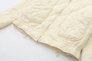 Detail of cream quilted jacket featuring metal zipper and curved large utility pockets