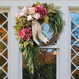 Pastel pink hydrangea wreath with autumn leaves and linen bow on a white farmhouse door